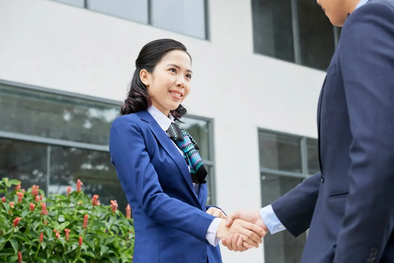 Toma de cintura para arriba de una mujer con vestimenta formal que saluda con un apretón de manos a su socio de negocios irreconocible.
